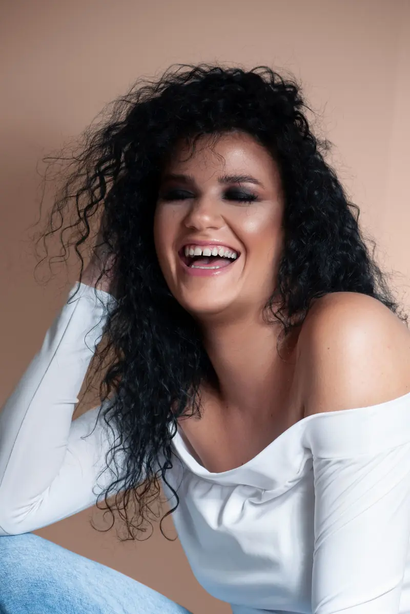 Vrouw met krullend haar lacht in een beige studio